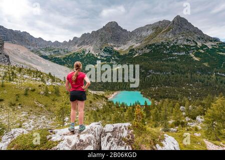 Jeune femme, randonneur se tient sur les rochers et regarde le lac turquoise de Sorapeiss et le paysage de montagne, Dolomites, Belluno, Italie Banque D'Images