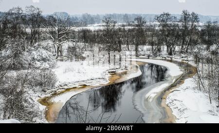 Vue sur la rivière non gelée. Paysage d'hiver. Neige sur le sol et arbres dans la forêt. Jour nuageux. Banque D'Images