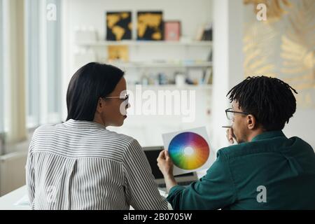 Vue arrière de deux jeunes concepteurs travaillant avec la palette de couleurs et en discutant en équipe à la table Banque D'Images