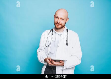 Un médecin souriant sympathique et sympathique, avec une tablette, regardant un appareil photo isolé sur le fond bleu Banque D'Images