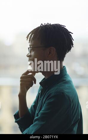 Vue latérale du jeune homme africain dans les lunettes debout et pensant à quelque chose Banque D'Images