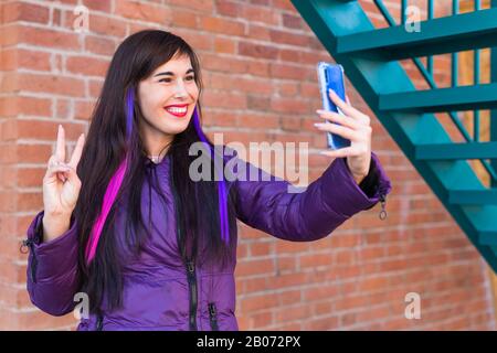 Technologies, concept urbain et populaire - Jolie fille avec de longs cheveux colorés prend un selfie sur le toit. Banque D'Images