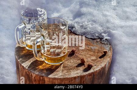Deux tasses de bière sur un tronc en bois dans la neige Banque D'Images