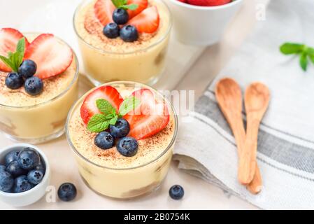 Tiramisu dessert exquis, faits maison dans les verres décorés de fraise, de bleuet, de menthe sur la table en bois blanc, Banque D'Images