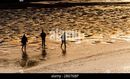 Une image panoramique de personnes marchant sur la plage de Porth à marée basse silhouetted par le soleil couchant à Newquay dans Cornwall. Banque D'Images