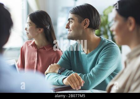 Jeunes gens d'affaires assis à la table regardant l'orateur et l'écoutant lors d'une réunion au bureau Banque D'Images