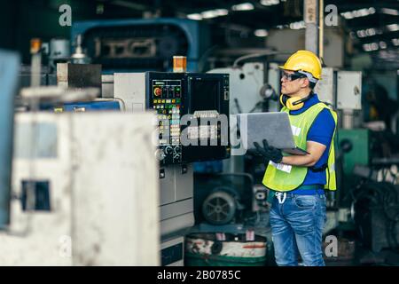 Un ingénieur asiatique programmant la machine en usine avec un ordinateur portable pour configurer le processus du programme. Banque D'Images