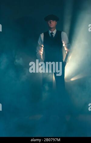 Homme d'affaires rétro avec casquette debout dans la chambre fumée. Banque D'Images