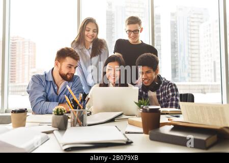 Des étudiants satisfaits multinationaux se réunissent à la bibliothèque, à l'aide d'un ordinateur portable Banque D'Images