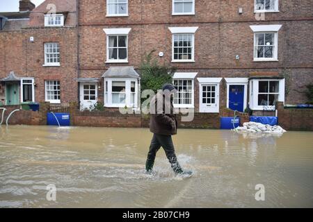 Un homme traverse les eaux d'inondation, tandis que les pompes et les barrières anti-inondation aident à empêcher l'eau d'inonder les maisons de Gloucester Road à Tewkesbury, dans le Gloucestershire, à la suite de la tempête Dennis. Banque D'Images