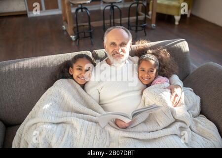 Grand-père et ses deux petites filles assis sur le canapé et se sentir à l'aise Banque D'Images