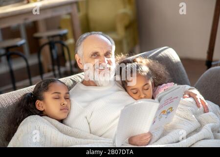 Deux filles dormant sur le canapé embrassant leur grand-père. Banque D'Images