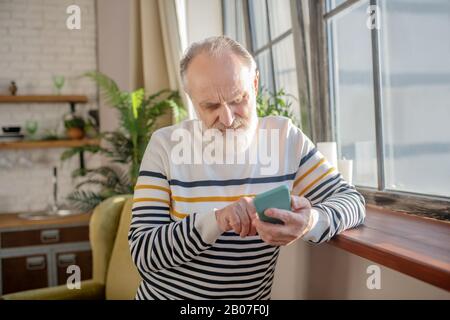 Homme barbu à poil gris dans un pull rayé en tapant un message Banque D'Images