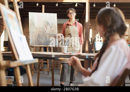 Jeune professeur debout près de la servante pointant sur l'image et tenant une leçon d'art pour les étudiants en studio d'art Banque D'Images