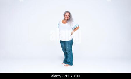 Femme senior souriante debout sur fond blanc. Gaie femme senior debout avec ses mains à la taille. Banque D'Images