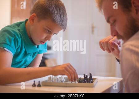 Jeune homme et son fils jouant aux échecs. Les deux pensent à leurs prochaines actions. Banque D'Images