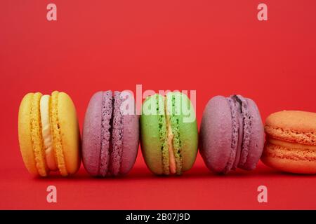 gâteaux de macarons ronds de couleur jaune, violet et vert sur fond rouge, dessert à la rangée, gros plan Banque D'Images