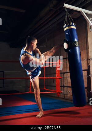 Kickboxer professionnel formation homme kickboxing dur et la préparation à la lutte, les coups de poing et de sac de boxe lourd près de l'anneau au club de santé Banque D'Images