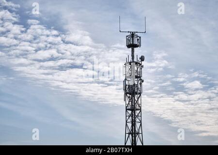 Gros plan du mât en réseau avec station de base pour les communications mobiles contre le ciel bleu avec nuages. Vu en Allemagne en février Banque D'Images