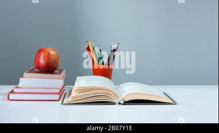 Porte-crayon orange, livre ouvert, journal, pages bronzées sur pile de livres sur table blanche avec pomme rouge. Empilage de livres. Retour au concept scolaire. Banque D'Images