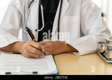 Certains gros plan femme médecin professionnel médical assis en salle d'examen clinique de l'hôpital de signer le document. Pas de récolte face Banque D'Images