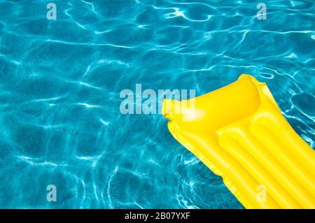 Lilo jaune vide flottant sur la piscine bleue en plein soleil Banque D'Images