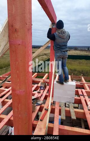 Menuisier sur l'installation du toit, marteau martelant clou dans la poutre en bois. Banque D'Images