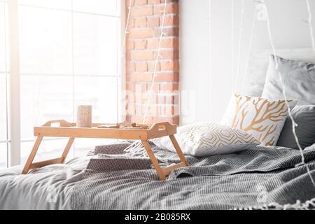 Une petite table de petit-déjeuner en bois se tient sur le lit dans la chambre, les draps gris, le soleil brille par le lever du soleil Banque D'Images