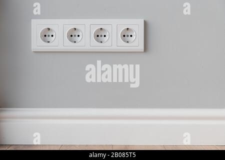 Prises européennes blanches sur mur gris en béton de style loft, avec plinthe en polyuréthane Banque D'Images