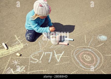 la petite fille dessine de la craie sur l'asphalte. enfant jouant en plein air en été. Banque D'Images