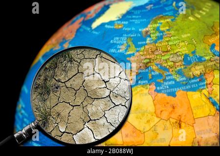 La terre craquelée par la sécheresse vu à travers une loupe tenu contre allumé globe terrestre Banque D'Images