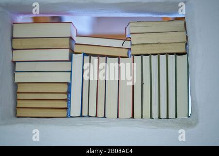 Détail de l'arrière de l'assortiment de livres dans une étagère blanche avec vue sur la chambre suivante dans un mur blanc texturé, ferme lumineux et amical Banque D'Images