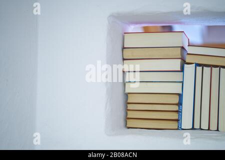Détail d'un assortiment de livres dans une étagère blanche dans un mur blanc texturé dans une pièce avec espace de copie, dos de livres Banque D'Images