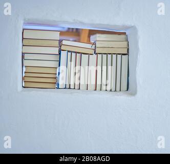 Détail ensoleillé brillant d'un assortiment de livres dans une étagère blanche dans un mur blanc texturé avec espace de copie, dos de livres Banque D'Images