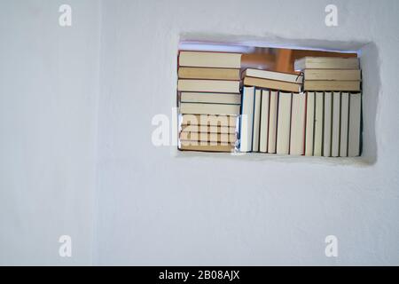 Détail ensoleillé lumineux d'un assortiment de livres dans une chambre avec mur blanc texturé dans une maison de campagne méditerranéenne, espace dans le mur avec vue sur le Banque D'Images