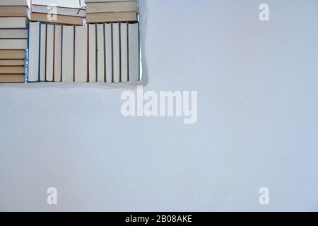 Détail ensoleillé lumineux d'un assortiment de livres dans une étagère blanche dans une pièce avec mur blanc texturé avec espace de copie, dos de livres Banque D'Images