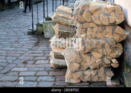 Le bois de chauffage sec dans une grille, empilé dans une pile, se trouve sur la rue de la ville ancienne, près du mur de la maison et du porche. Banque D'Images