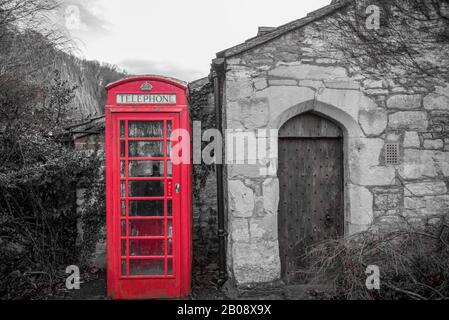 Boîte téléphonique rouge à côté d'une porte de l'église dans le château de Coombe, Wiltshire en noir et blanc Banque D'Images