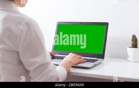 Une femme travaille dans un bureau blanc sur un ordinateur portable avec un écran vert. Banque D'Images