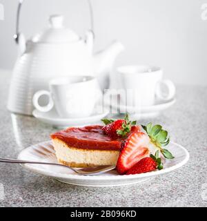 tranche d'un cheesecake avec une couche de confiture de fraises sur le dessus servi sur une plaque blanche avec des baies fraîches comme garniture Banque D'Images