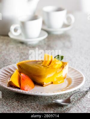 tranche d'un cheesecake fraîchement cuit surmontée d'une compote de mangue servie sur une plaque blanche Banque D'Images