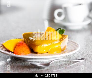 tranche d'un cheesecake fraîchement cuit surmontée d'une compote de mangue servie sur une plaque blanche Banque D'Images