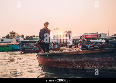 Un homme vietnamien local sur son bateau au lever du soleil regardant le marché flottant à Can Tho, au Vietnam. Banque D'Images