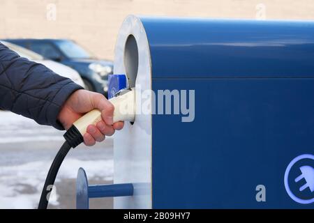 Concept de transport écologique. Station de chargeur électrique de voiture installée dans le parking. La main tient le chargeur pour les voitures électriques. Banque D'Images