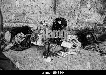 Une femme ouvre une boîte de tiffin pour avoir de la nourriture tandis qu'une femme âgée dort derrière elle, sur un pavé près de l'église Sainte Marie à Bangalore. Les personnes démunies comme celles-ci sont ramassées et envoyées aux maisons des débutants dans les villes. Bangalore, Karnataka, Inde. 27 Décembre 2010. Une des images de l'histoire de la photo, Criminalisant la pauvreté, par Ayush Ranka. Banque D'Images