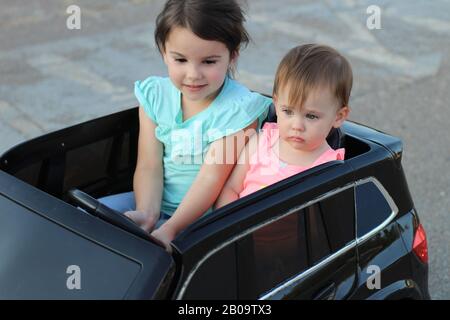 Deux superbes filles vont dans une grande voiture jouet sur l'asphalte de la rue de la ville. Conduite en plein air dans une attraction estivale pour les enfants Banque D'Images