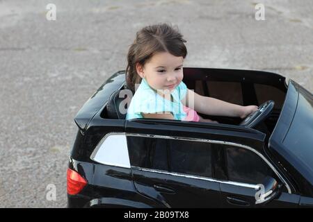 Deux superbes filles vont dans une grande voiture jouet sur l'asphalte de la rue de la ville. Conduite en plein air dans une attraction estivale pour les enfants Banque D'Images