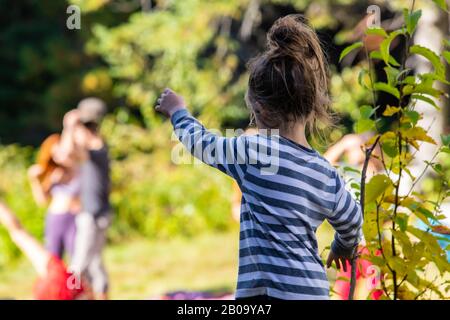 Un foyer sélectif tiré de derrière une jeune fille de 5 ans portant un haut rayé bleu et blanc, et pointant vers des personnes floues en arrière-plan Banque D'Images