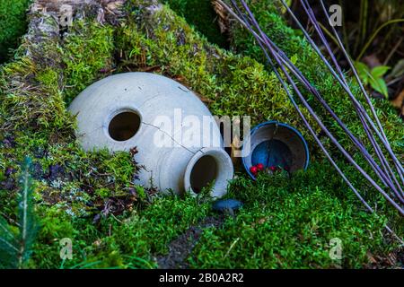 Gros plan d'une maison de fées magique dans une forêt, avec une bosse couverte de mousse, une urne de pierre renversée, des baies rouges, des brindilles. Copier l'espace vers la droite Banque D'Images