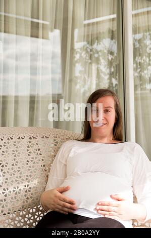 Femme enceinte de 30 ans se posant dans un fauteuil dans une galerie Banque D'Images